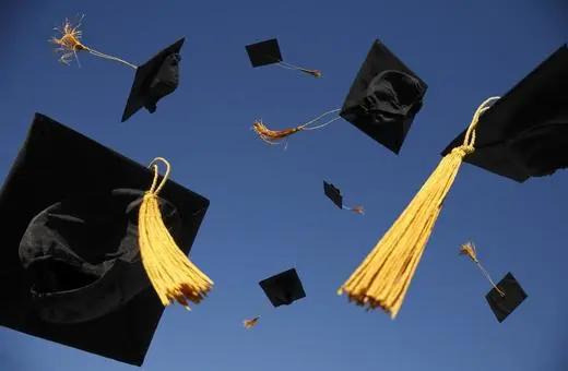 A group of black graduation caps with gold tassels soaring against a clear blue sky, symbolizing celebration and achievement.