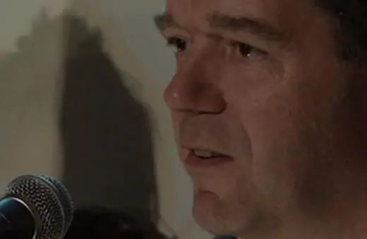 A man speaking into a microphone, focused on delivering a message, with soft lighting highlighting his expression.