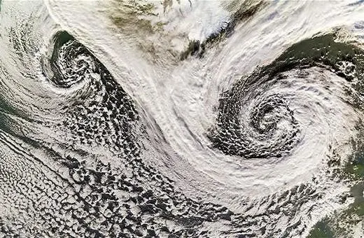 Satellite image of two contrasting weather systems in the ocean, showing spiraling cloud formations indicative of cyclonic activities.