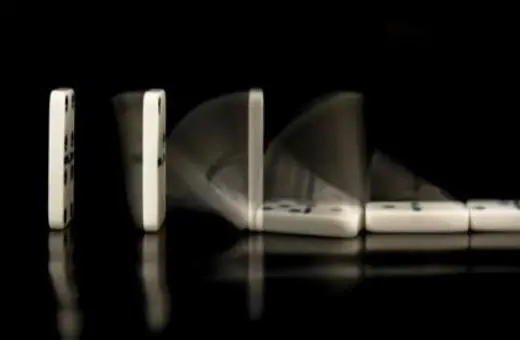 A series of white dominoes in motion, illustrating a cascading effect as one topples into the next against a black background.