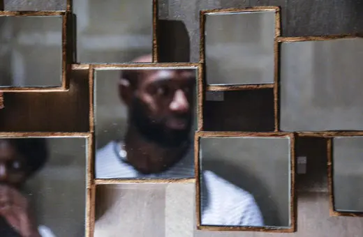 A fragmented mirror arrangement reflecting a person, creating an abstract and artistic representation of their silhouette in a dimly lit space.