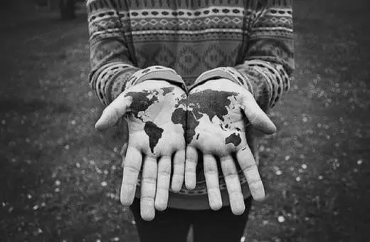 A person holds their hands out, displaying a black and white map of the world painted on their palms.