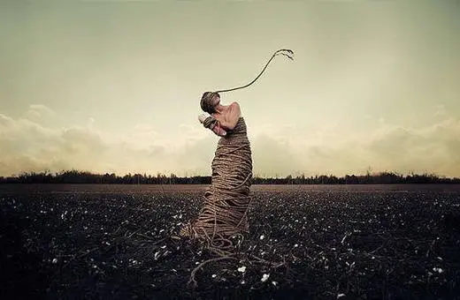 A figure wrapped in rope stands in an open field under a dramatic sky, conveying themes of entrapment and struggle.