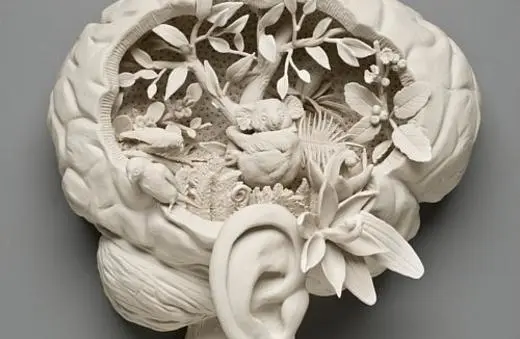 A sculptural representation of a brain featuring intricate carvings of trees, flowers, and animals, emphasizing the connection between nature and cognition.