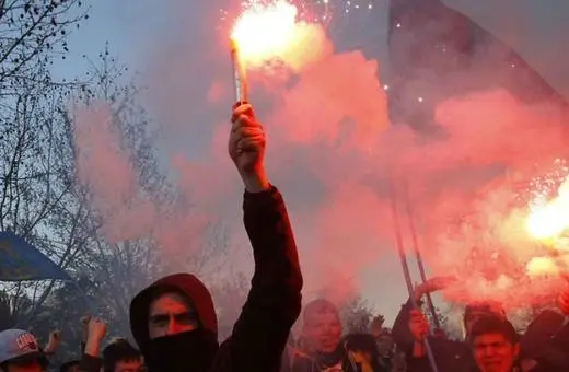 A group of protesters holding flares and flags, surrounded by smoke, demonstrating in a spirited atmosphere.