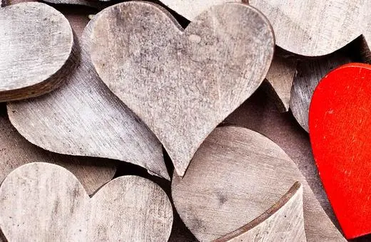 A collection of wooden heart shapes in various shades, with one vibrant red heart standing out among the muted tones.
