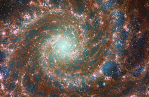 A vibrant, colorful depiction of a spiral galaxy, showcasing swirling patterns of stars, dust, and glowing gas against a darker cosmic background.