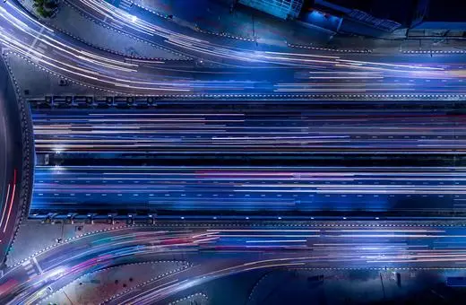 Aerial view of a bustling highway interchange at night, showcasing vibrant light trails from moving vehicles amidst the urban landscape.