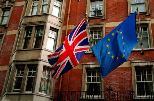 A British flag and a European Union flag displayed outside a brick building, symbolizing the relationship between the UK and the EU.