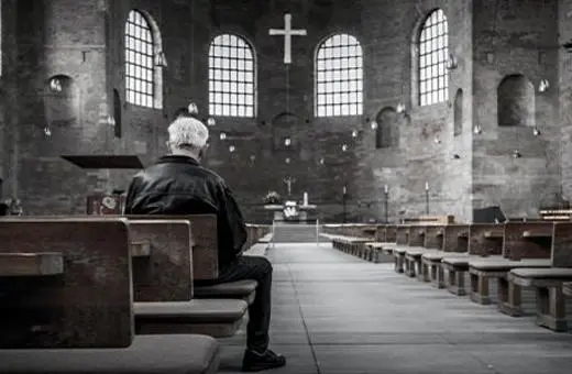 A middle-aged man with glasses gestures while speaking, surrounded by plants and sunflowers, indicating a thoughtful or passionate discussion.