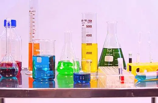 A collection of various laboratory glassware filled with colorful liquids, including beakers, flasks, and test tubes, arranged on a metallic table.