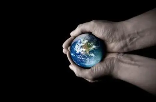 A pair of hands gently cradles a small globe, symbolizing the Earth, against a dark background.