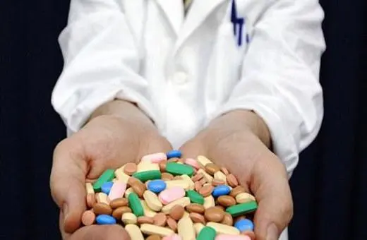 A person in a lab coat holds a large assortment of colorful pills and tablets in their hands, emphasizing a focus on medication and health.