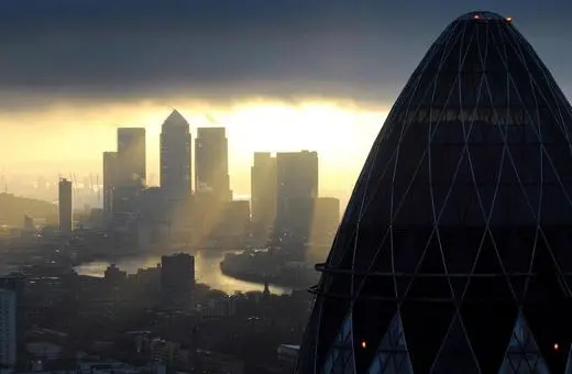 A dramatic skyline view of London featuring the iconic Gherkin building with the River Thames flowing and dark clouds overhead.