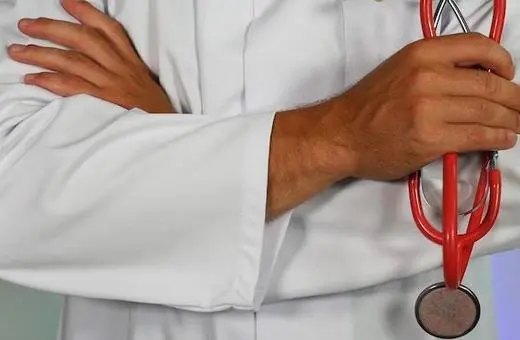 A medical professional in a white coat holds a red stethoscope with arms crossed, symbolizing healthcare and physician authority.