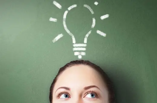A close-up of a person's face with lightbulb doodle above their head, symbolizing ideas and creativity against a green chalkboard background.