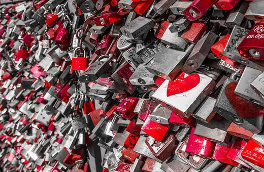 A vibrant collection of padlocks in various colors, predominantly red, attached to a fence or structure, symbolizing love and commitment.