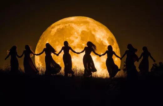Silhouettes of women holding hands in a circle against a large, glowing full moon in the background.