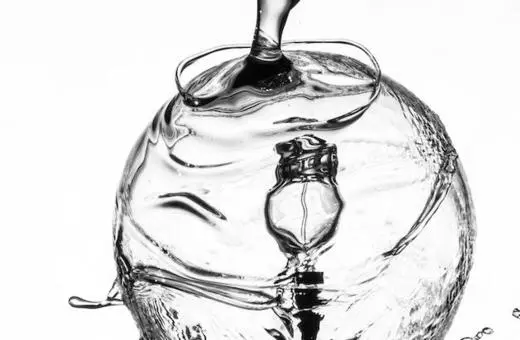 Close-up of a water droplet creating ripples on a transparent globe, showcasing fluid dynamics and reflections in monochrome.