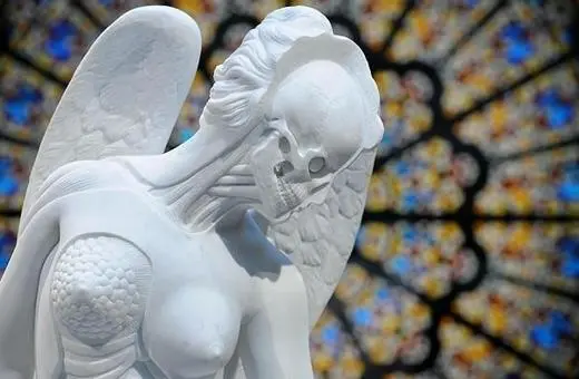 A skeletal angel sculpture contrasts with a vibrant stained glass window, showcasing intricate details of the figure and the colorful backdrop.