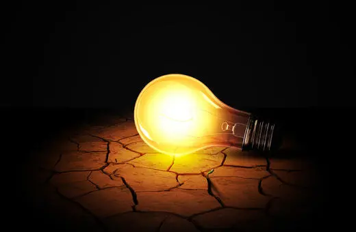 A glowing light bulb sits on a cracked, dry surface, illuminating the surrounding darkness with a warm yellow light.